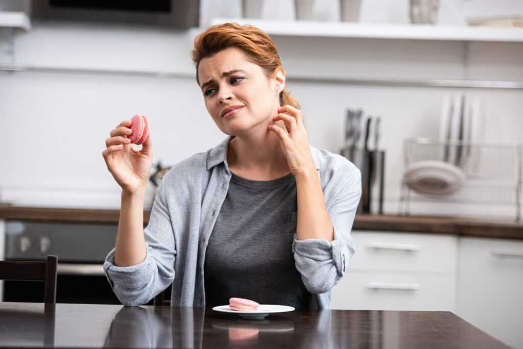 woman looking at pink dessert while scratching neck